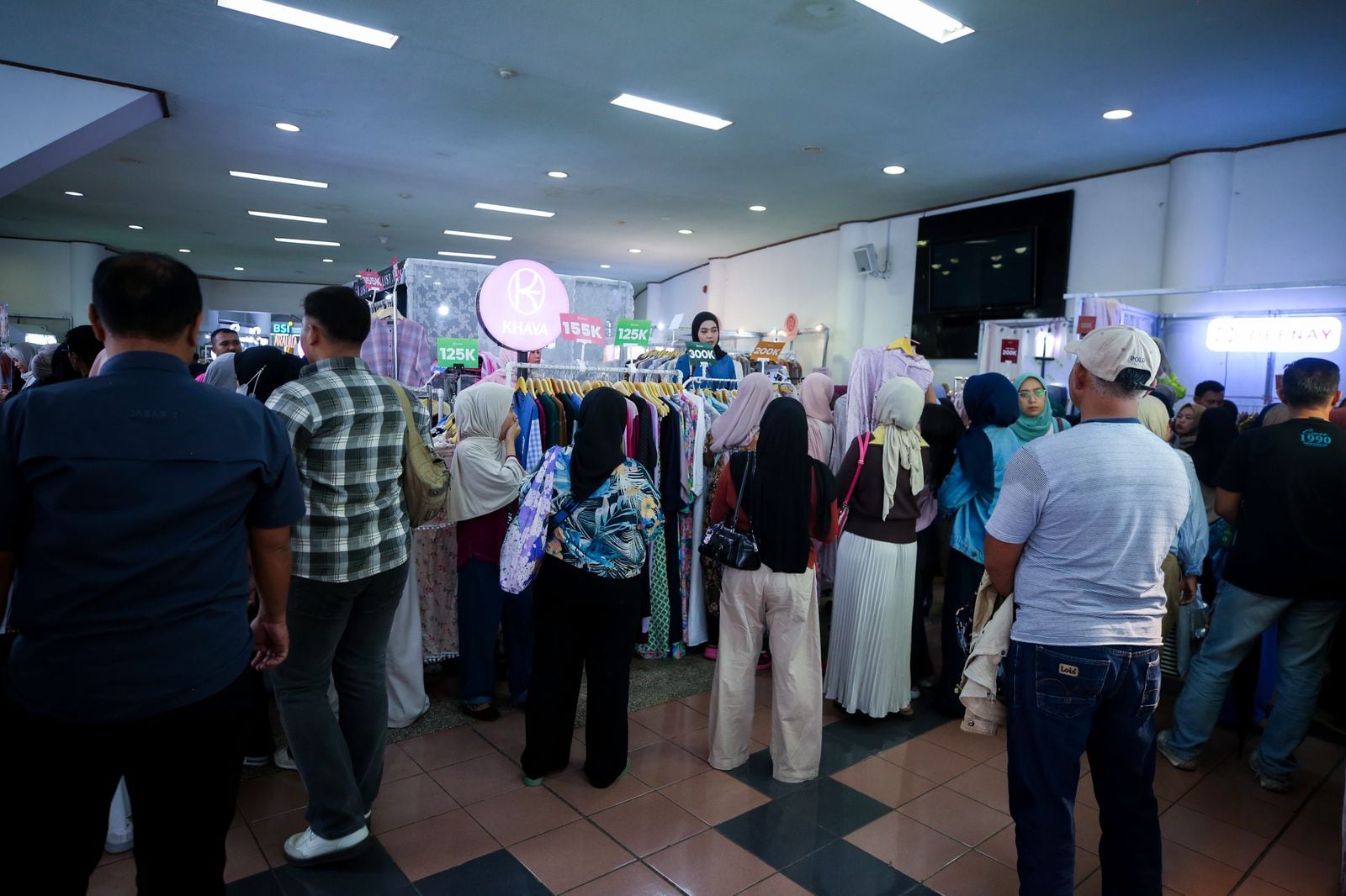 Shoppers in hijabs and modest separates browse rails of dresses and tunics at a brand booth during Indonesia Hijabfest 2026 at Gedung Sabuga, Bandung