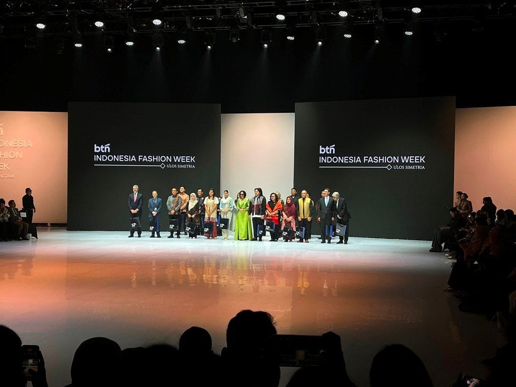 Guests and organisers stand on the runway before screens reading BTN Indonesia Fashion Week, Ulos Simetria, on opening night