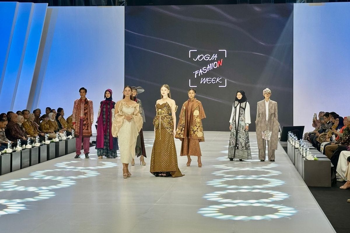 Models in batik and woven-textile looks line the runway beneath the Jogja Fashion Week logo at the opening of the 2025 edition