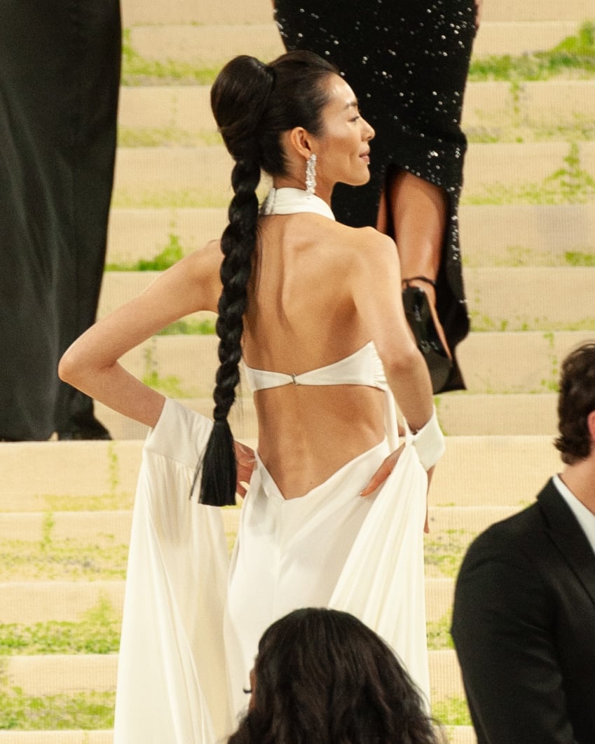 Liu Wen, seen from behind with a long braided ponytail, in a white draped Michael Kors Collection gown with wrist swags at the 2026 Met Gala