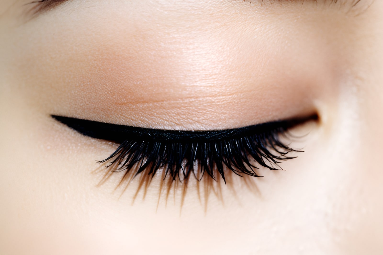 Macro of long black lashes and a fine eyeliner flick on a closed eye