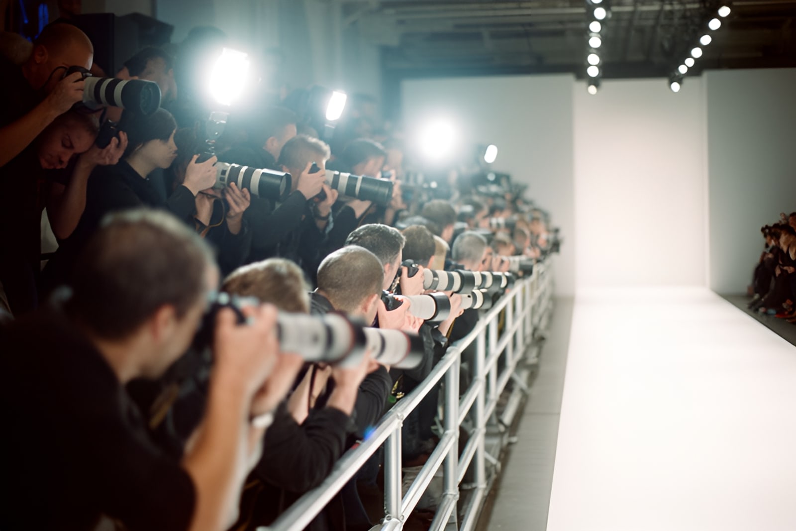 Photographers with long lenses on tiered risers at the end of a fashion runway